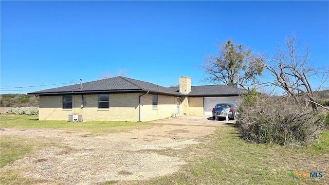 back of house featuring brick siding, a chimney, concrete driveway, a lawn, and an attached garage