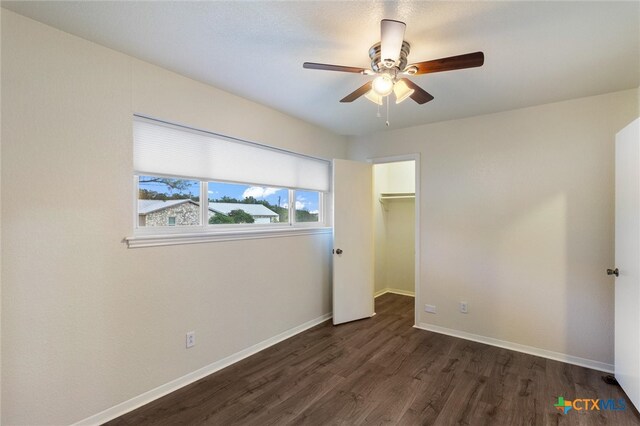 unfurnished bedroom featuring ceiling fan, a spacious closet, dark wood-type flooring, and a closet