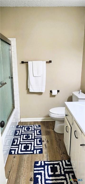 full bathroom with hardwood / wood-style floors, bath / shower combo with glass door, vanity, a textured ceiling, and toilet