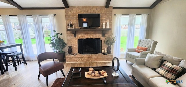 living room with a brick fireplace, a wealth of natural light, beam ceiling, and light hardwood / wood-style flooring