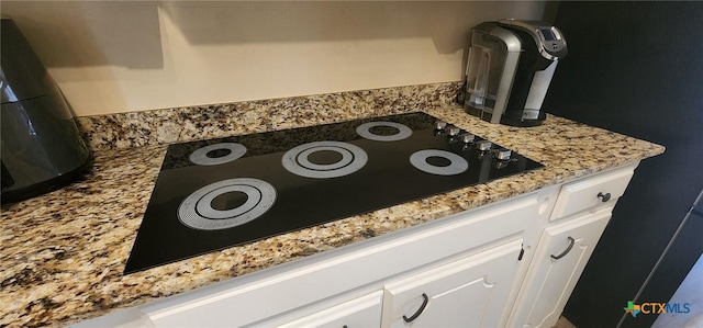 room details featuring white cabinetry, light stone countertops, and black electric stovetop