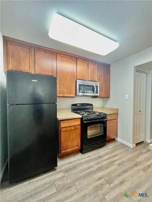 110 Rush Hvn, San Marcos, TX 78666 - kitchen featuring brown cabinets, light wood-type flooring, black appliances, light countertops, and baseboards