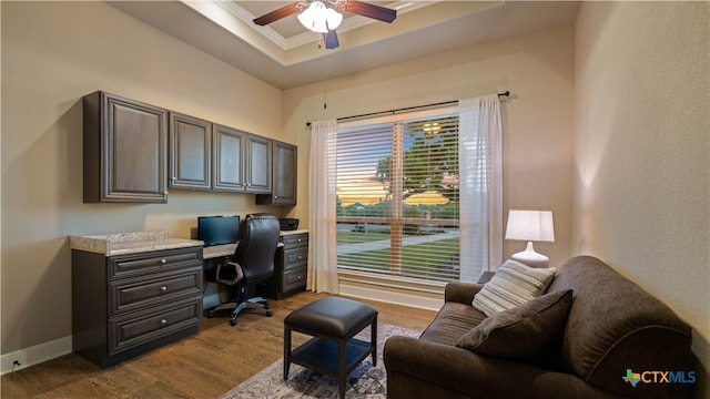 office area with a ceiling fan, wood finished floors, built in study area, ornamental molding, and a tray ceiling