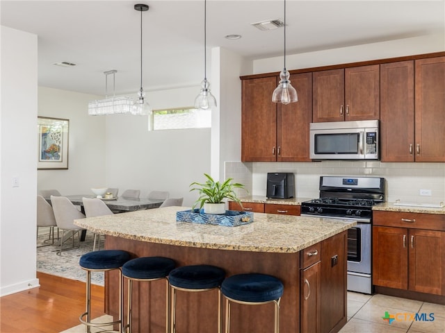 1200 Marcy St, Austin, TX 78745 - kitchen with appliances with stainless steel finishes, a kitchen island, a breakfast bar area, tasteful backsplash, and light stone countertops