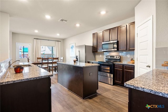 kitchen featuring light stone countertops, appliances with stainless steel finishes, a kitchen island with sink, and sink