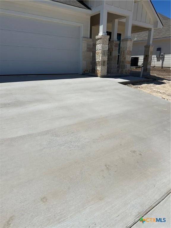 exterior space featuring board and batten siding, an attached garage, stone siding, and concrete driveway