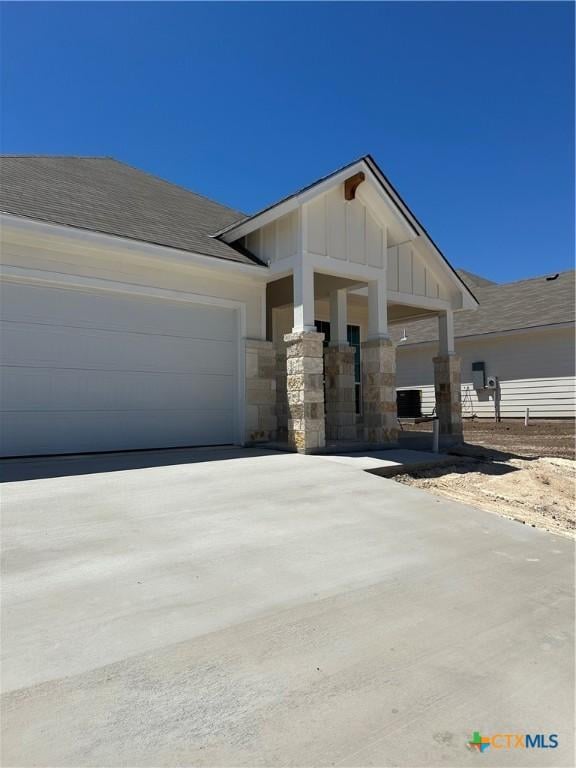 view of front of house with an attached garage, driveway, stone siding, and board and batten siding