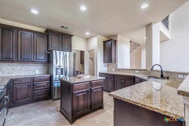 2933 Countryside Path, Seguin, TX 78155 - kitchen with stainless steel fridge, light stone countertops, dark brown cabinets, decorative backsplash, and recessed lighting