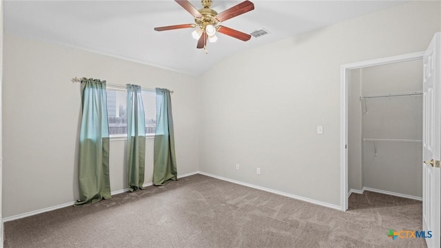 unfurnished bedroom featuring carpet flooring, a walk in closet, visible vents, vaulted ceiling, and a closet