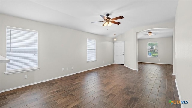 empty room featuring arched walkways, ceiling fan, dark wood-style floors, and baseboards