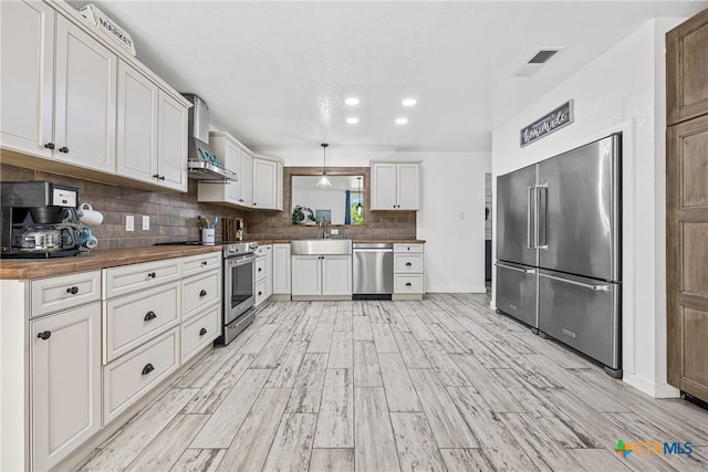 1213 Indian Trl, Salado, TX 76571 - kitchen featuring stainless steel appliances, wall chimney range hood, wooden counters, light wood-style floors, and recessed lighting