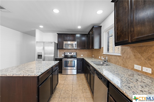 kitchen featuring stainless steel appliances, sink, light stone countertops, a kitchen island, and decorative backsplash