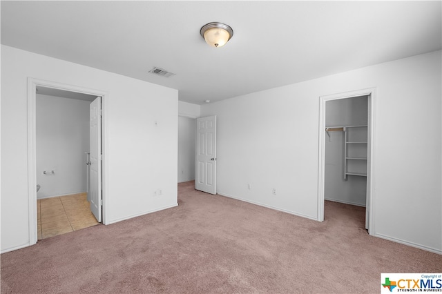 unfurnished bedroom featuring ensuite bath, light carpet, a walk in closet, and a closet