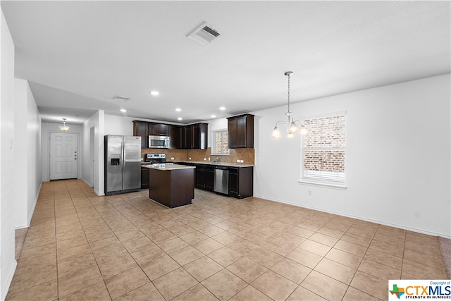 kitchen featuring dark brown cabinetry, appliances with stainless steel finishes, a chandelier, a kitchen island, and pendant lighting