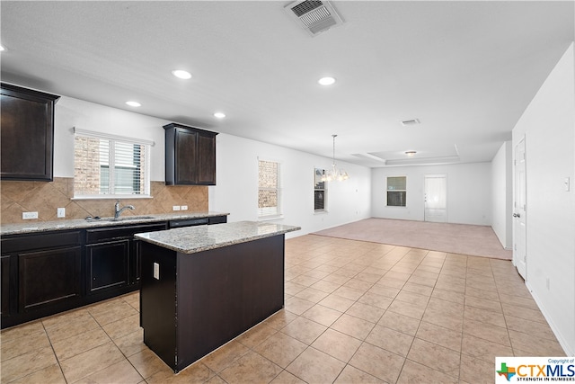 kitchen with a chandelier, light tile patterned flooring, a kitchen island, backsplash, and light stone countertops