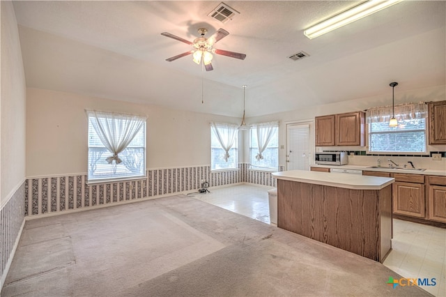 kitchen with sink, ceiling fan with notable chandelier, a kitchen island, pendant lighting, and vaulted ceiling