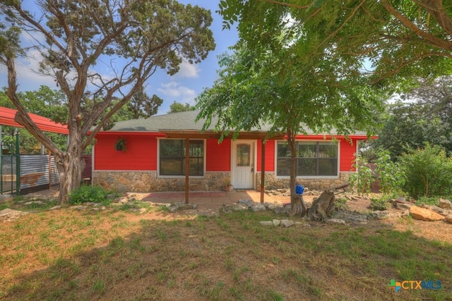 view of front of house with stone siding, a front yard, and a patio