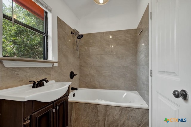 bathroom with tiled shower / bath, tile walls, vanity, and vaulted ceiling