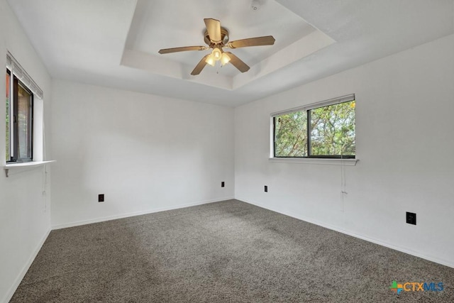 carpeted spare room with baseboards, a raised ceiling, and ceiling fan