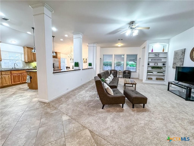 living area with built in shelves, light tile patterned floors, light colored carpet, ceiling fan, and ornate columns