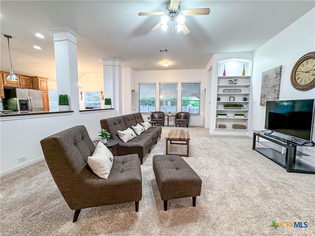 living room featuring baseboards, ceiling fan, built in features, light colored carpet, and ornate columns