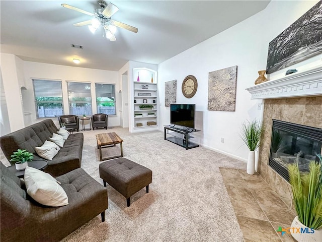 carpeted living area featuring visible vents, built in shelves, a ceiling fan, baseboards, and a tile fireplace