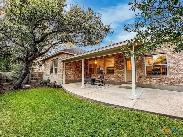 rear view of property with a patio, a lawn, brick siding, and fence