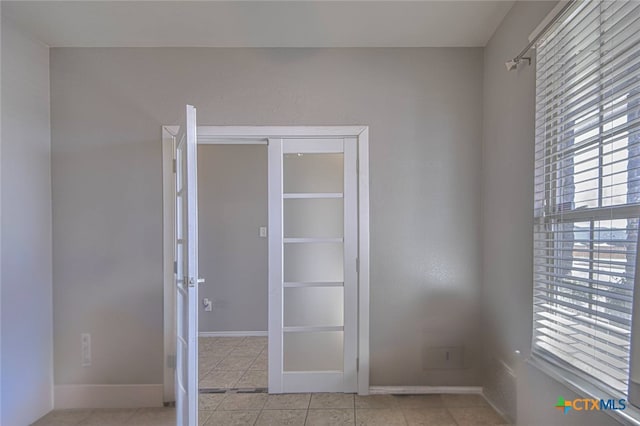 empty room with light tile patterned floors, baseboards, and a healthy amount of sunlight