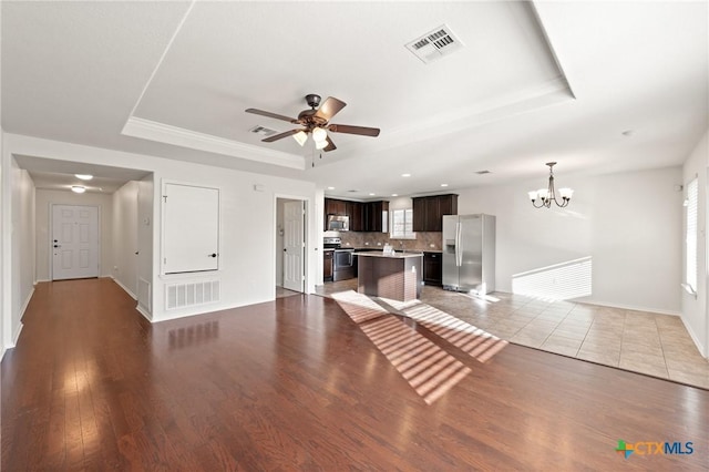 unfurnished living room with ceiling fan with notable chandelier, a raised ceiling, and light hardwood / wood-style flooring