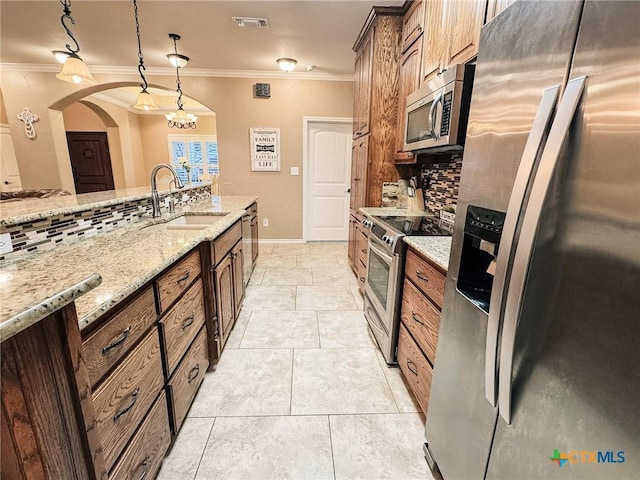 kitchen with pendant lighting, sink, stainless steel appliances, crown molding, and light stone countertops