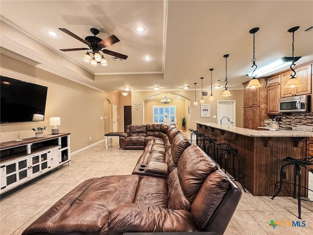 living room featuring sink, crown molding, light tile patterned floors, a raised ceiling, and ceiling fan