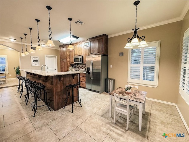 kitchen with a kitchen bar, decorative light fixtures, a center island with sink, ornamental molding, and appliances with stainless steel finishes