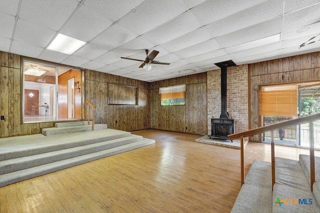 unfurnished living room featuring light wood-type flooring, wooden walls, a drop ceiling, and plenty of natural light