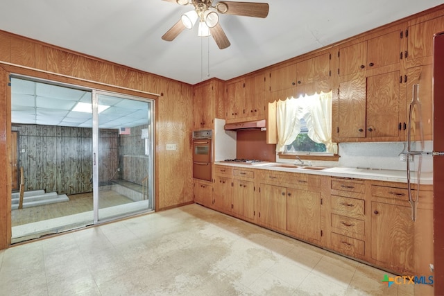 kitchen featuring wood walls, ceiling fan, sink, and white gas stovetop