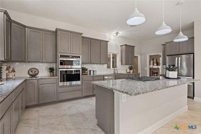 kitchen featuring a center island, a sink, stainless steel appliances, backsplash, and light stone counters