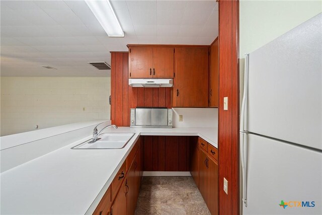 kitchen featuring freestanding refrigerator, brown cabinetry, visible vents, under cabinet range hood, and light countertops