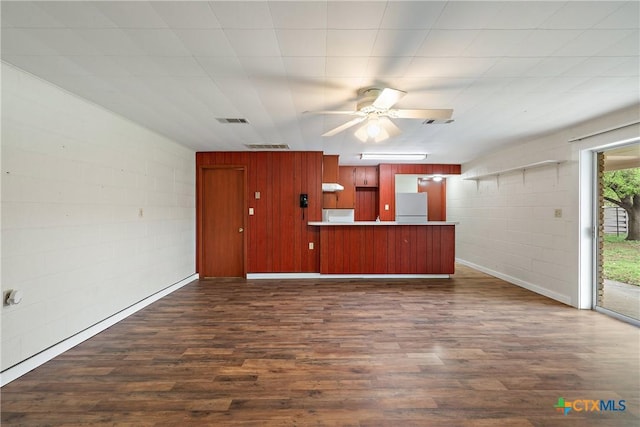 unfurnished living room with ceiling fan, dark wood-style floors, visible vents, and concrete block wall