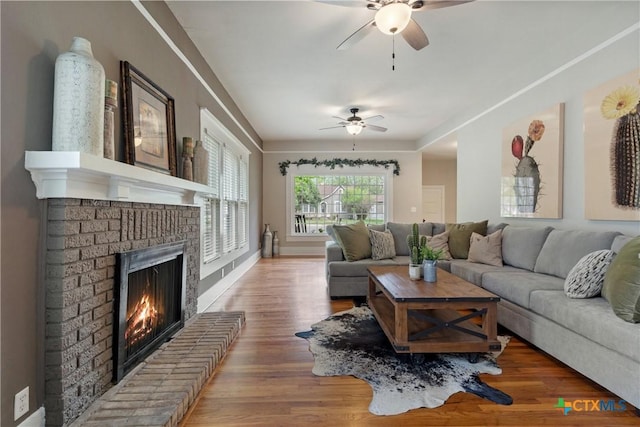 living room with wood finished floors, a ceiling fan, and a brick fireplace