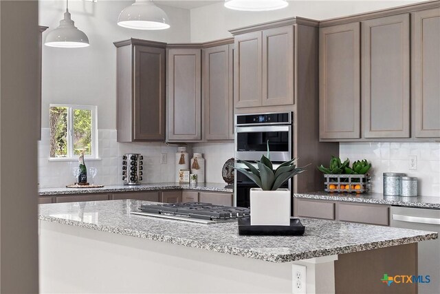 kitchen with appliances with stainless steel finishes, pendant lighting, decorative backsplash, a kitchen island, and light stone counters