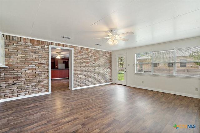 empty room with visible vents, ceiling fan, wood finished floors, and brick wall