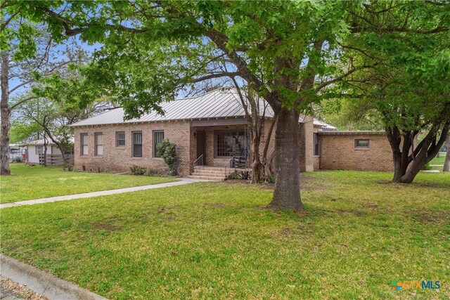 single story home with a standing seam roof, a front yard, metal roof, and brick siding