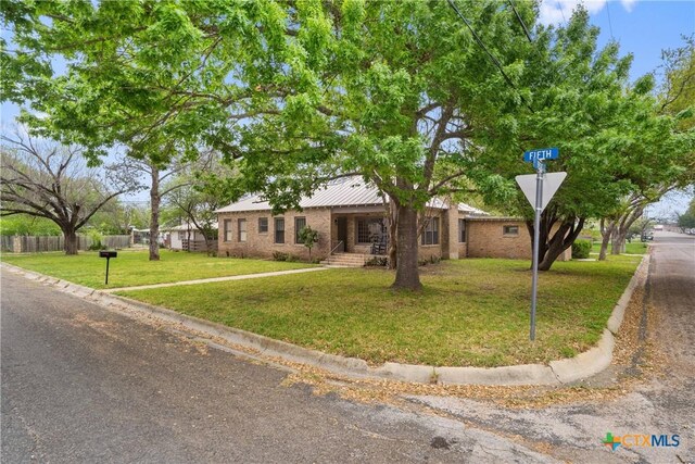 ranch-style home featuring metal roof, a front yard, and fence