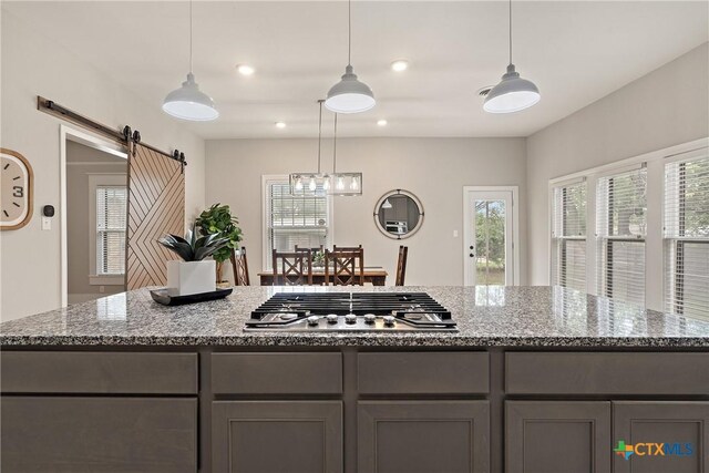 kitchen with stone counters, a barn door, stainless steel gas cooktop, and gray cabinets