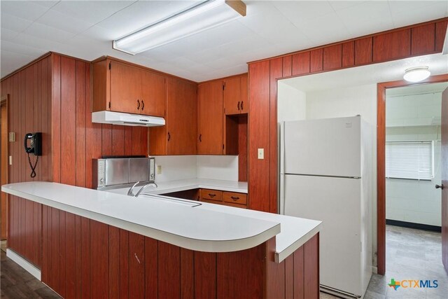 kitchen featuring freestanding refrigerator, a peninsula, under cabinet range hood, light countertops, and a sink