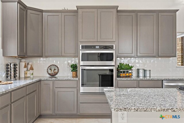 kitchen with decorative backsplash, gray cabinetry, light stone countertops, and double oven