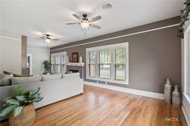 living area with baseboards, a fireplace, light wood-style floors, visible vents, and ceiling fan