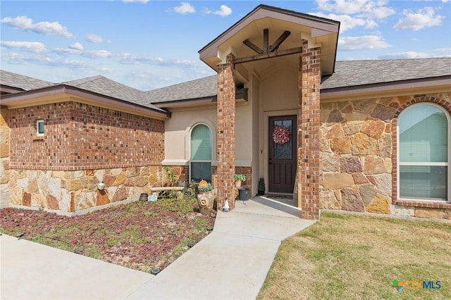 doorway to property featuring stone siding, a shingled roof, brick siding, and stucco siding