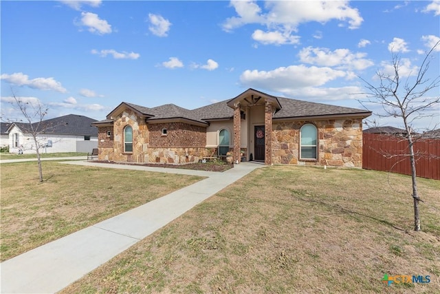 view of front facade featuring roof with shingles, stone siding, a front yard, and fence