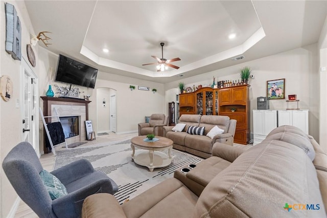 living area with a tray ceiling, arched walkways, visible vents, baseboards, and ceiling fan