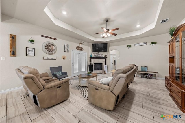living room featuring a tray ceiling, visible vents, a ceiling fan, arched walkways, and baseboards